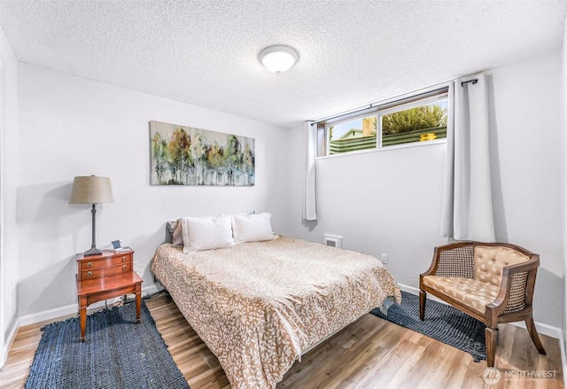 bedroom featuring a textured ceiling, baseboards, and wood finished floors