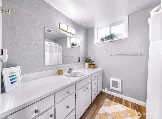 bathroom with visible vents, a textured ceiling, a textured wall, and wood finished floors