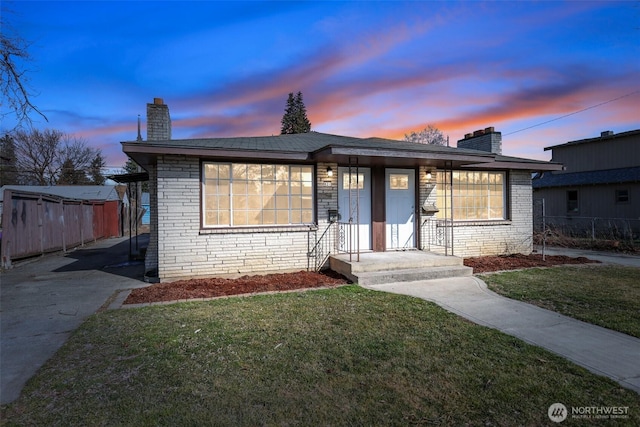 view of front of property featuring brick siding, a front yard, a chimney, and fence