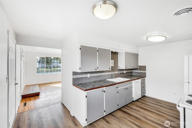 kitchen featuring dark countertops, visible vents, tasteful backsplash, white appliances, and a sink