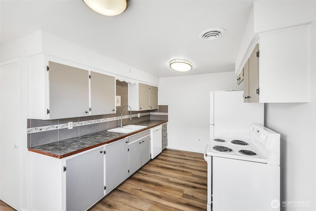 kitchen with dark countertops, visible vents, tasteful backsplash, white appliances, and a sink