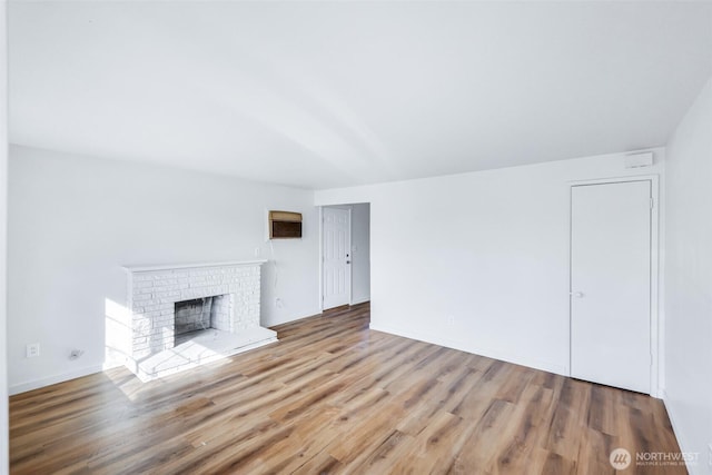 unfurnished living room featuring a brick fireplace, wood finished floors, and baseboards