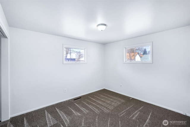 spare room featuring visible vents, baseboards, and dark carpet