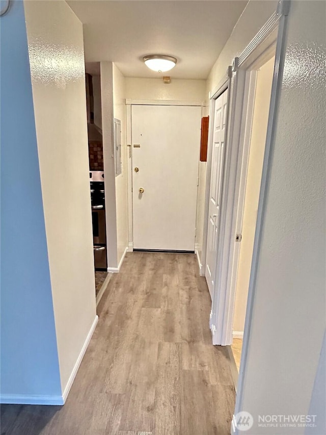 corridor with baseboards and light wood-style floors