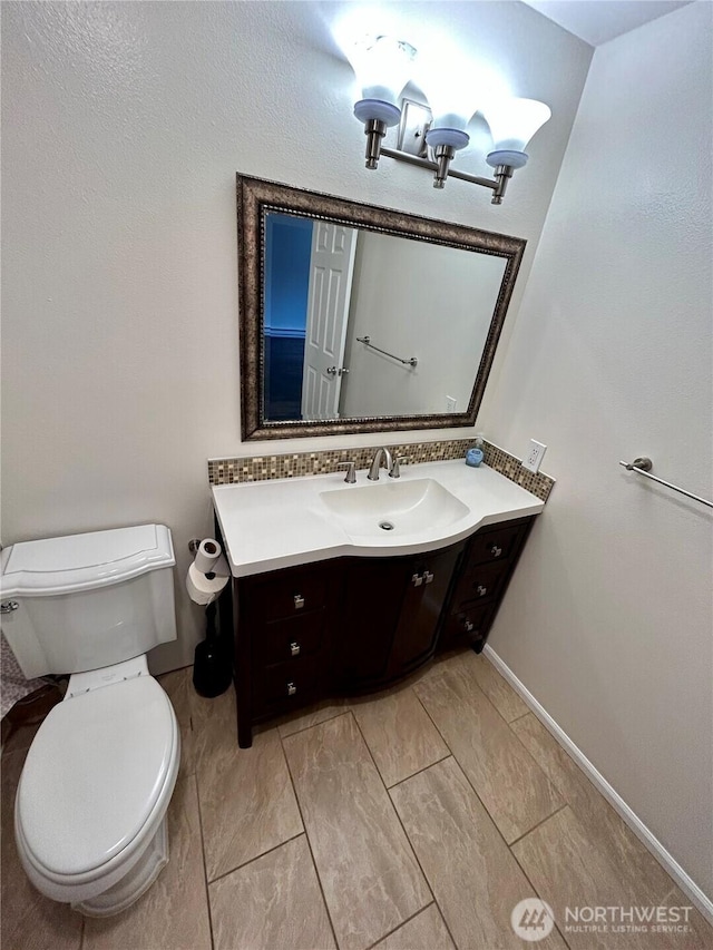 bathroom featuring toilet, vanity, and baseboards