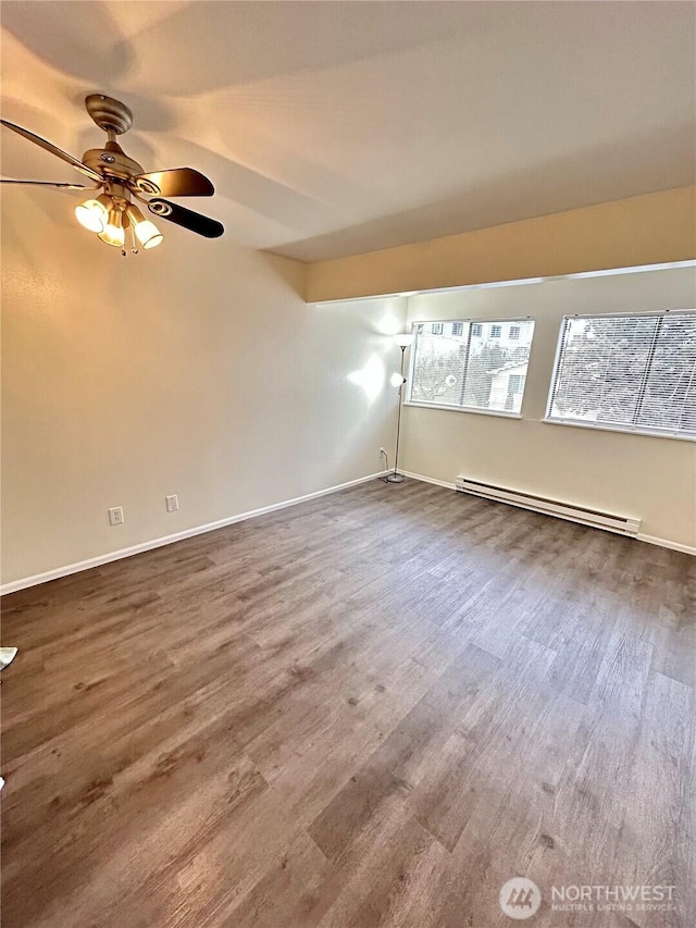 spare room featuring ceiling fan, a baseboard heating unit, baseboards, and wood finished floors