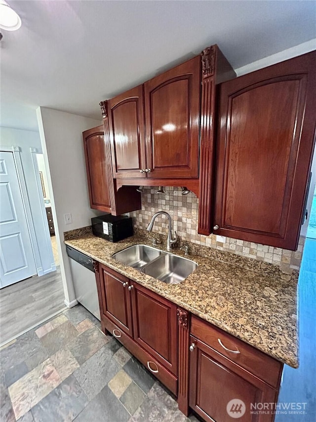 kitchen featuring baseboards, a sink, decorative backsplash, stone finish flooring, and stainless steel dishwasher