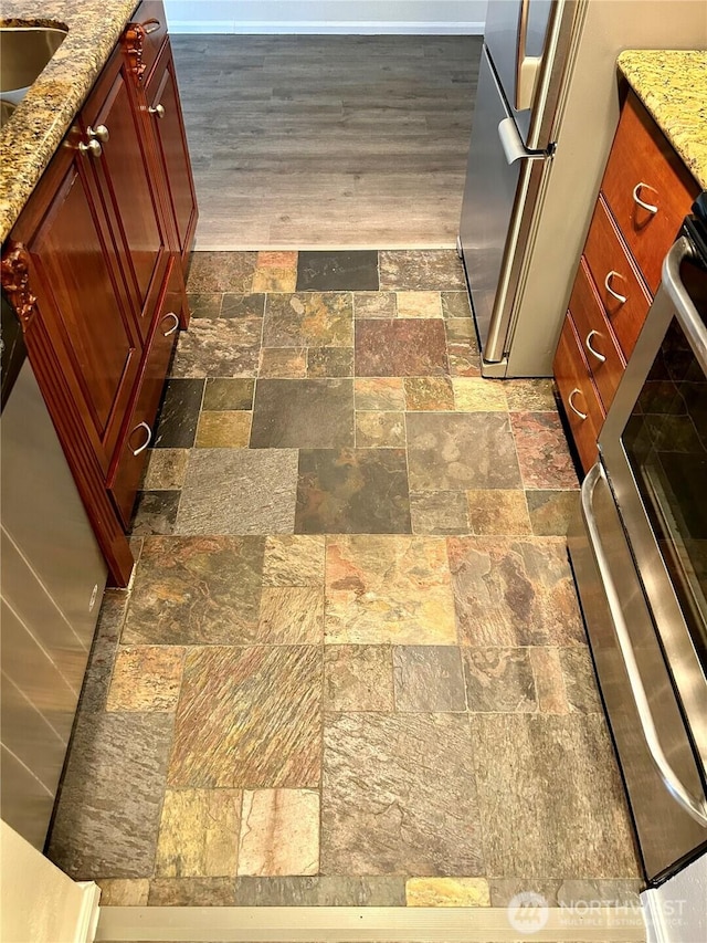 room details with stove, light stone countertops, freestanding refrigerator, and reddish brown cabinets