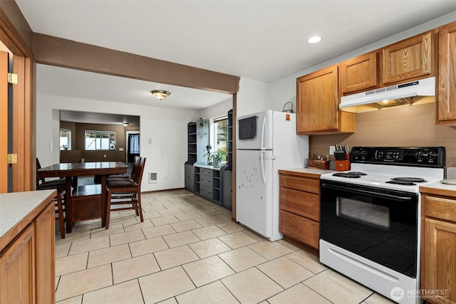 kitchen with freestanding refrigerator, light countertops, electric stove, under cabinet range hood, and brown cabinets