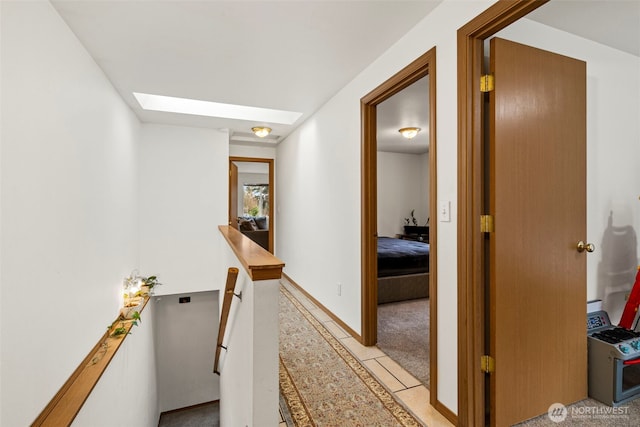 corridor with baseboards, an upstairs landing, light carpet, and a skylight