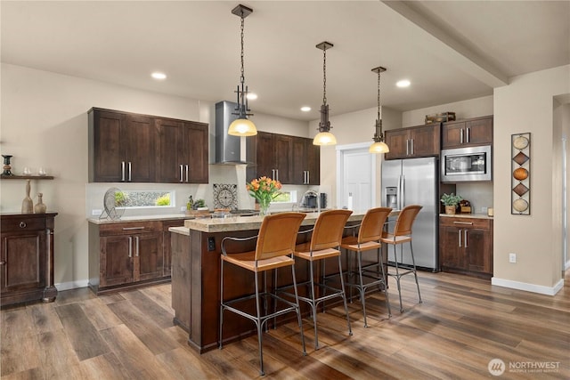 kitchen featuring dark wood-style floors, appliances with stainless steel finishes, wall chimney exhaust hood, and a breakfast bar