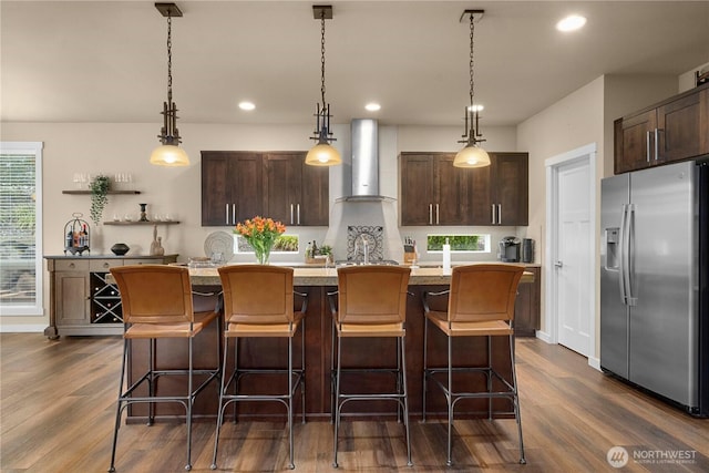 kitchen with dark brown cabinets, a healthy amount of sunlight, wall chimney exhaust hood, and stainless steel fridge with ice dispenser