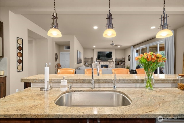 kitchen with a sink, visible vents, light stone counters, and a stone fireplace