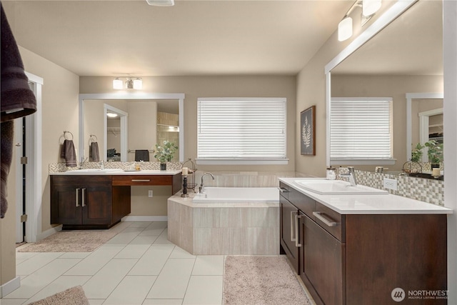 full bath featuring two vanities, tile patterned floors, a bath, and a sink