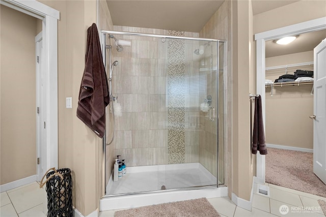 bathroom featuring tile patterned floors, a stall shower, a walk in closet, and baseboards