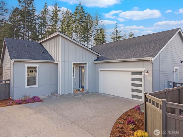 view of front of house with driveway, an attached garage, roof with shingles, and fence