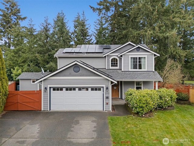 traditional-style house featuring a front lawn, aphalt driveway, roof mounted solar panels, fence, and a garage