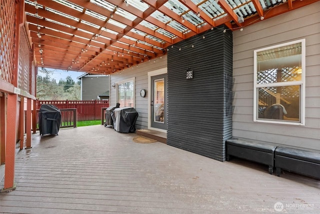 wooden deck with area for grilling, fence, and a pergola