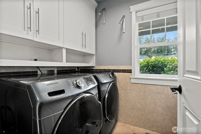 clothes washing area with washing machine and clothes dryer, cabinet space, tile patterned flooring, wainscoting, and tile walls