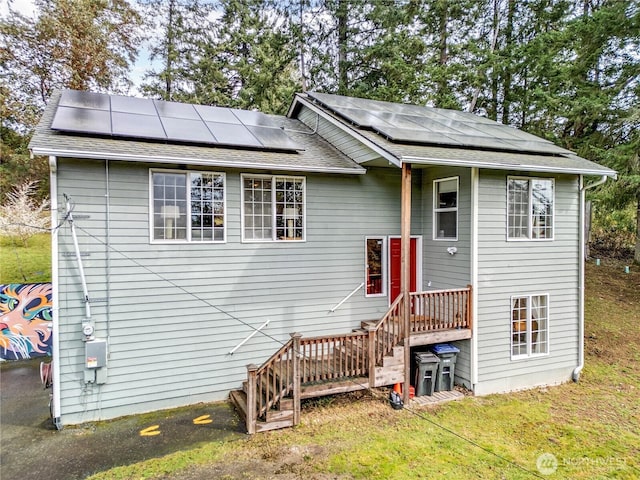 view of front facade with roof mounted solar panels, a shingled roof, and a front yard