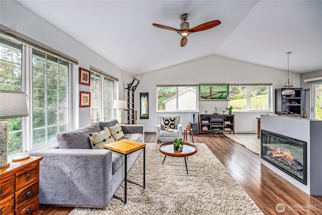 living area featuring wood finished floors, baseboards, a ceiling fan, vaulted ceiling, and a glass covered fireplace