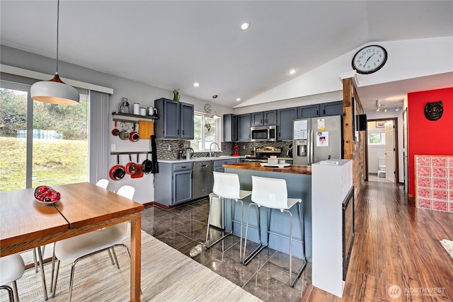 kitchen with a kitchen island, a kitchen bar, lofted ceiling, decorative backsplash, and appliances with stainless steel finishes