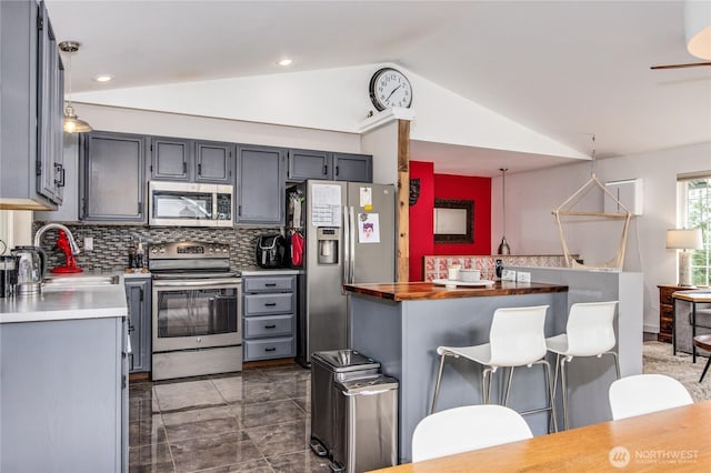 kitchen with lofted ceiling, gray cabinets, a sink, appliances with stainless steel finishes, and tasteful backsplash