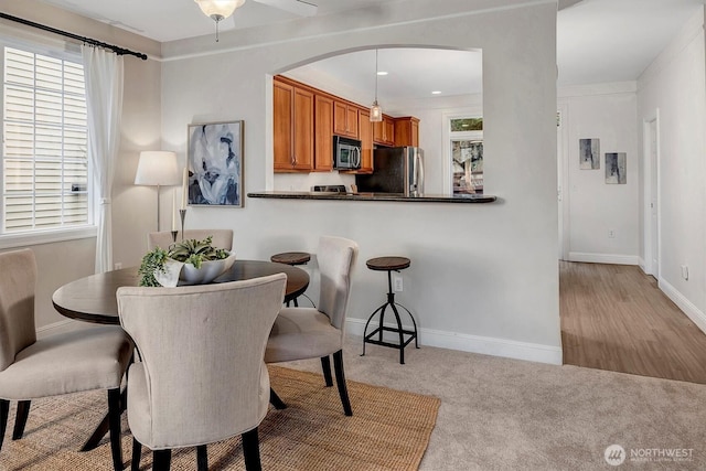 dining room featuring arched walkways, light colored carpet, and baseboards