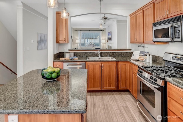 kitchen featuring light wood finished floors, dark stone countertops, appliances with stainless steel finishes, a ceiling fan, and a sink