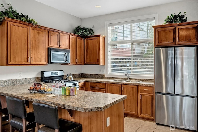 kitchen featuring a sink, a kitchen breakfast bar, appliances with stainless steel finishes, brown cabinetry, and light tile patterned floors