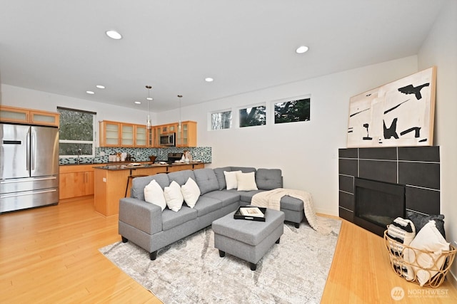 living area with recessed lighting, light wood-type flooring, a wealth of natural light, and a tiled fireplace