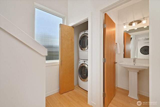 washroom featuring baseboards, stacked washer and clothes dryer, wood finished floors, and laundry area