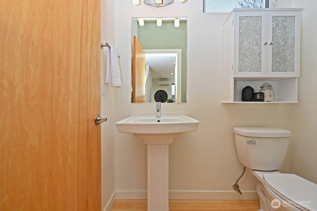 half bath featuring baseboards, toilet, and wood finished floors