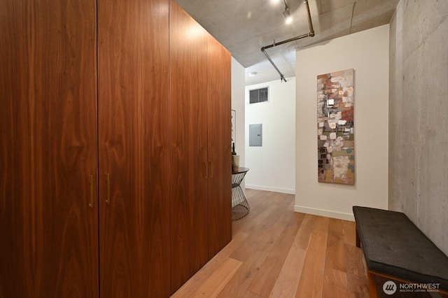 hall featuring light wood-type flooring, visible vents, track lighting, electric panel, and baseboards