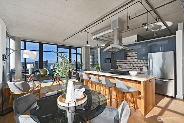 kitchen with tasteful backsplash, light wood-type flooring, light countertops, freestanding refrigerator, and island range hood