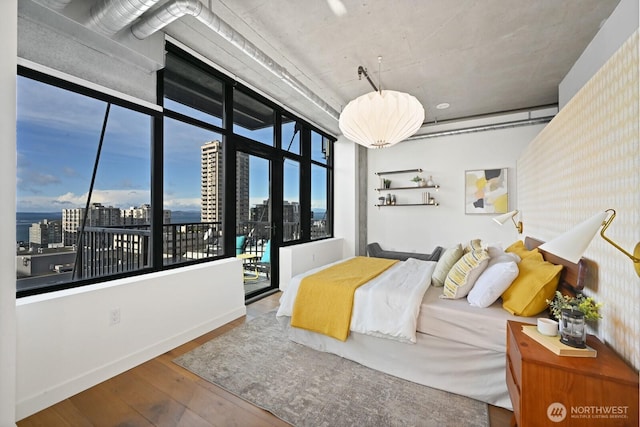 bedroom with baseboards, a view of city, wood finished floors, and access to exterior