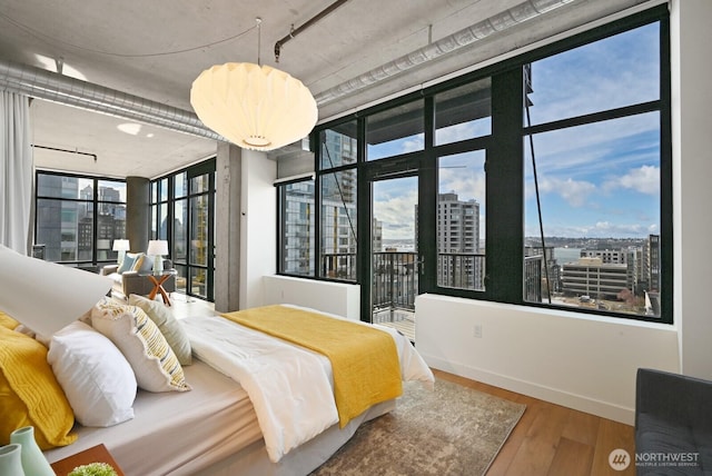 bedroom featuring access to exterior, a view of city, wood finished floors, and baseboards