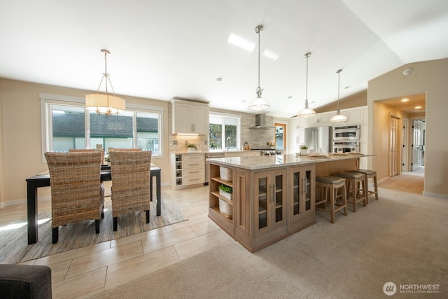 kitchen with a spacious island, lofted ceiling, stainless steel appliances, wall chimney exhaust hood, and open shelves