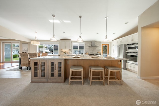 kitchen featuring wall chimney exhaust hood, glass insert cabinets, light colored carpet, and appliances with stainless steel finishes