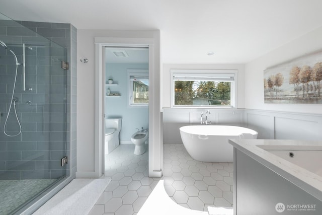 bathroom featuring tile patterned flooring, a shower stall, a bidet, wainscoting, and a freestanding tub