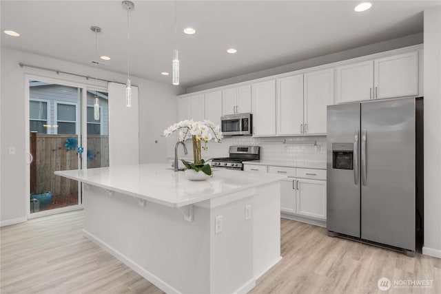 kitchen with tasteful backsplash, an island with sink, light wood-style flooring, stainless steel appliances, and white cabinetry