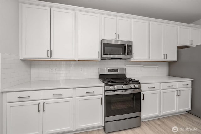 kitchen with backsplash, light countertops, light wood-style flooring, white cabinets, and stainless steel appliances