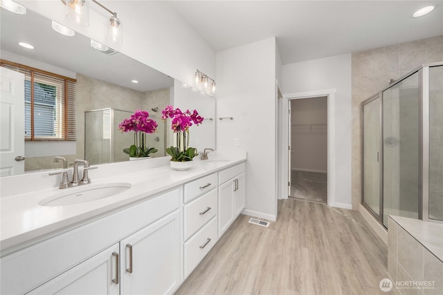 full bathroom featuring visible vents, a walk in closet, a stall shower, a sink, and double vanity