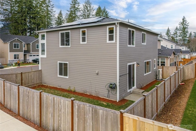 view of side of property with ac unit, a fenced backyard, a residential view, and roof mounted solar panels