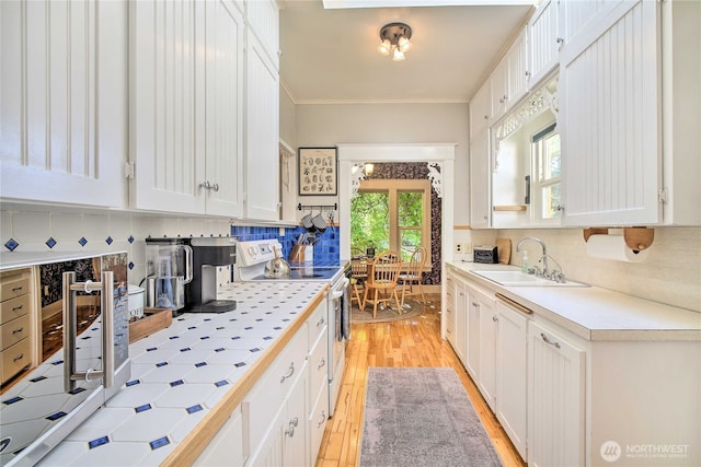 kitchen with white electric range, a sink, backsplash, tile countertops, and white cabinets