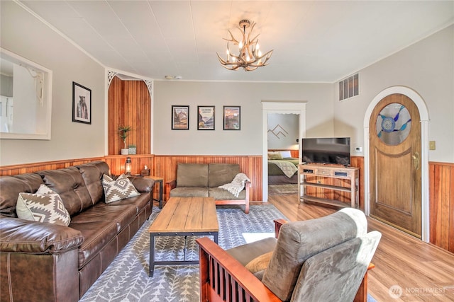 living room featuring visible vents, a wainscoted wall, wood finished floors, arched walkways, and a notable chandelier