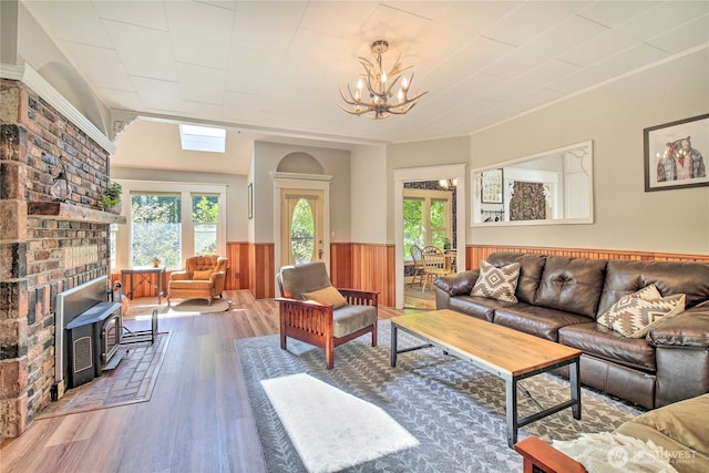 living area featuring a wood stove, wood finished floors, a wainscoted wall, and a chandelier