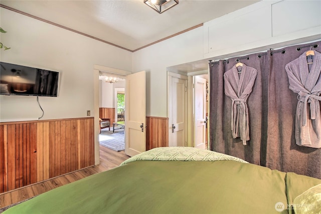 bedroom with wooden walls, wood finished floors, wainscoting, and ornamental molding