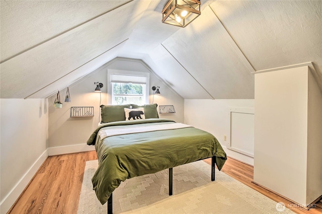 bedroom featuring vaulted ceiling, a textured ceiling, baseboards, and wood finished floors