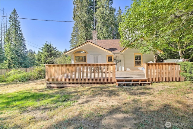 rear view of property featuring a wooden deck, a lawn, and a chimney